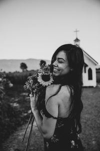 Woman smiling holding flowers with a chapel and mountains in the background