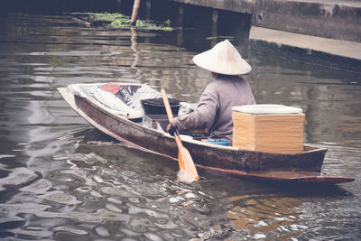 Rear view of man rowing while sitting in boat on canal