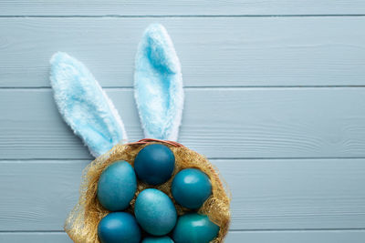Easter flat lay with blue eggs in the basket and funny bunny ears on light blue wooden background