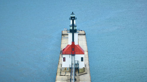 Lighthouse by sea against clear blue sky