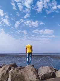 Rear view of man standing on rock by sea against sky