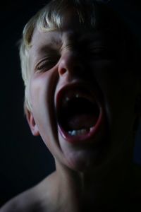 Close-up of boy shouting against black background