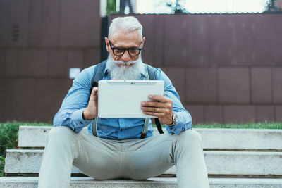 Senior hipster holding digital tablet sitting on steps