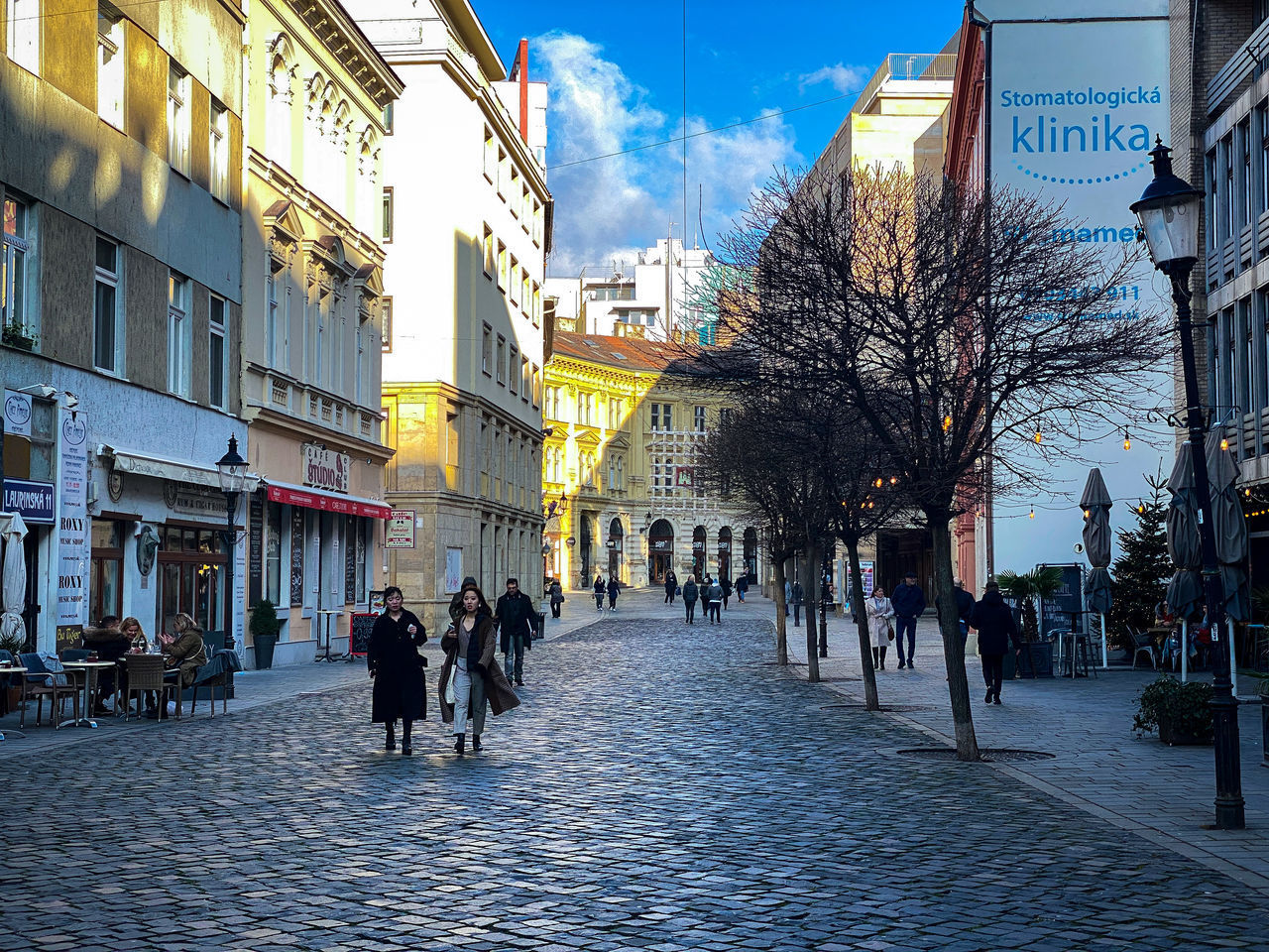 PEOPLE WALKING ON STREET AMIDST CITY BUILDINGS