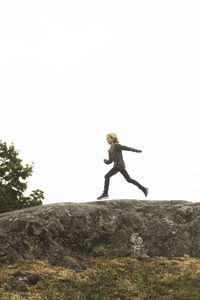 Full length side view of girl running on rock formation against clear sky