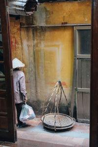 Rear view of mid adult man holding bag while standing at alley seen through doorway