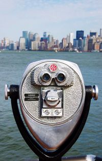 Close-up of coin-operated binoculars by sea against buildings in city