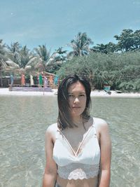 Portrait of young woman standing against river during sunny day