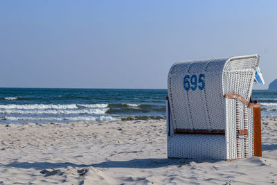 Hooded beach chair on shore against clear sky