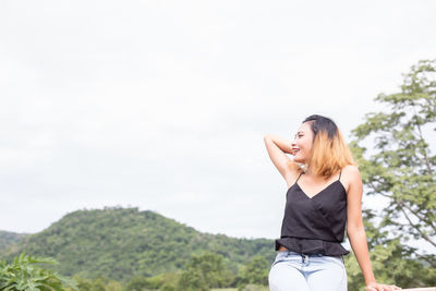 Young woman looking away while standing against sky