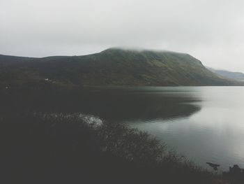 Scenic view of lake and mountains against sky during foggy weather