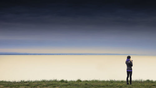 Rear view of woman standing on grassy field in front of river