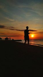 Silhouette man standing on beach against sky during sunset