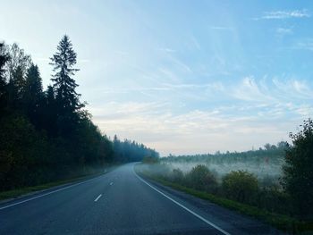 Empty road along trees and against sky