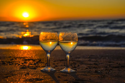 Wineglass on beach against sky during sunset