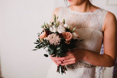 Midsection of bride holding flower bouquet against wall