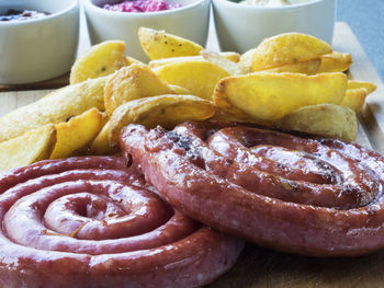 High angle view of fresh curled sausages with potato wedges on serving board