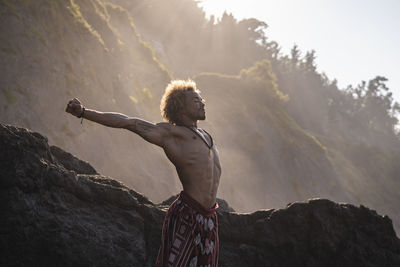 Shirtless young man stretching arms while standing at beach