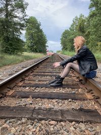 Side view of woman sitting on railroad track against sky