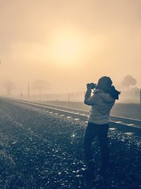 Rear view of mid adult man photographing while standing on field at sunset