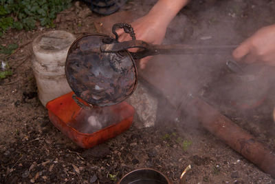 Cropped hands of woman tinning kitchen utensil on field