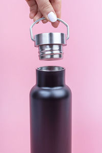 Female hands close a metal reusable bottle for water on pink background