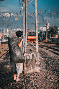 Rear view of man standing on railroad track against sky