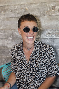 Smiling woman wearing sunglasses looking away while sitting against wall at restaurant