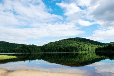 Scenic view of calm lake amidst mountain against cloudy sky