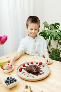 A boy decorates a heart-shaped chocolate cake for mother's day with fresh berries. valentine's day