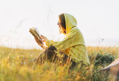 Side view of woman reading book sitting on field