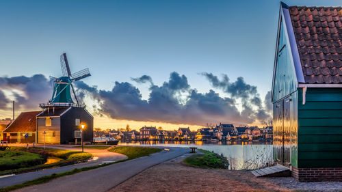 Traditional windmill by building against sky during sunset