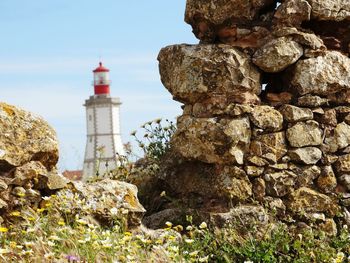 Lighthouse amidst rocks and buildings against sky