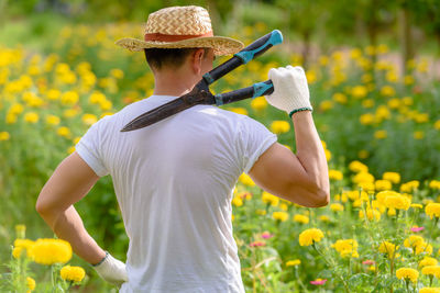 Rear view of man holding pliers while standing on flowering field