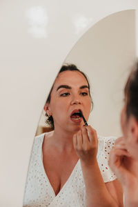 Mirror photo of beautiful young woman putting on makeup