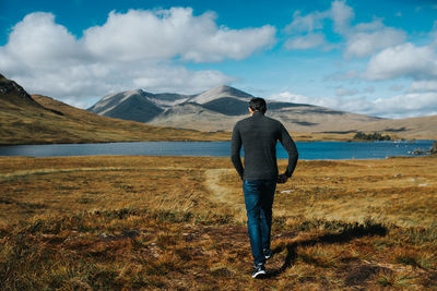 Rear view of man walking at lakeshore against sky