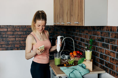 Sportswoman preparing vegan smoothie from green vegetables and celery in the kitchen