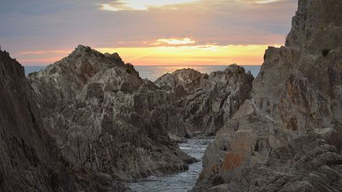 Panoramic view of rock formations in sea against sky during sunset
