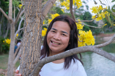 Portrait of a smiling young woman against tree trunk