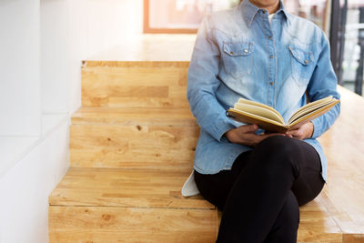 Low section of woman reading book at home