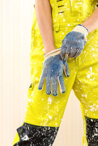 Cropped image of woman in dirty coveralls wearing gloves paintbrush while standing against wall