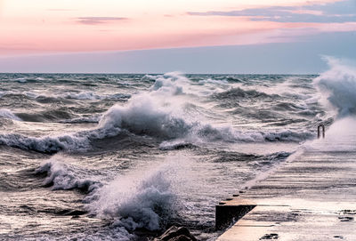 Waves splashing on shore against sky during sunset