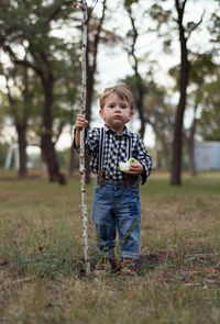 Full length of boy holding apple and stick while standing on field