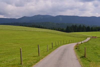 Scenic view of road amidst field against sky