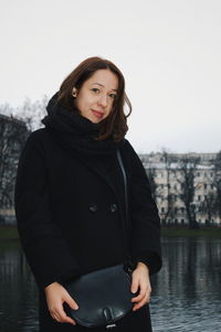 Portrait of young woman standing against river