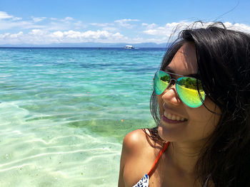 Portrait of young woman in sunglasses at beach against sky