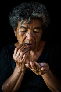 Close-up senior woman eating pills against black background
