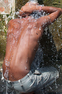 Rear view of shirtless man bathing outdoors