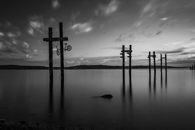 Silhouette wooden posts in lake against sky