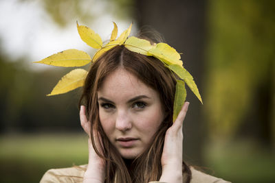 Close-up portrait of young woman holding leaf crown
